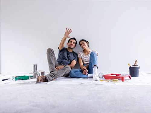 Couple sitting on floor with paint supplies discussing home improvement.