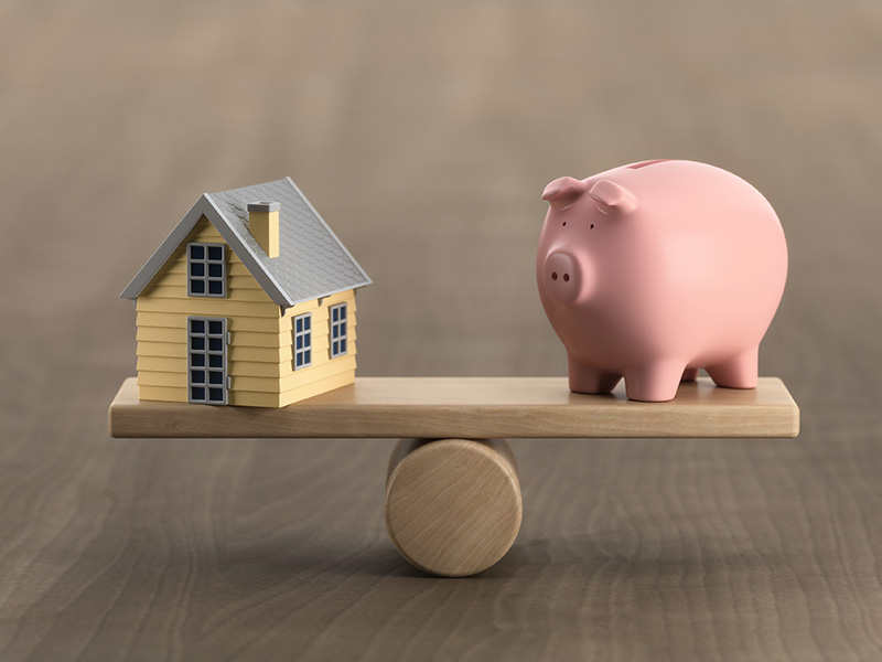 miniature model house and toy pig balanced on a wooden scale. Budget balance concept.